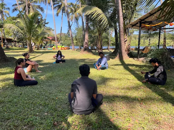 Guests seated in a circle on the grass listening to the facilitator, with the river behind