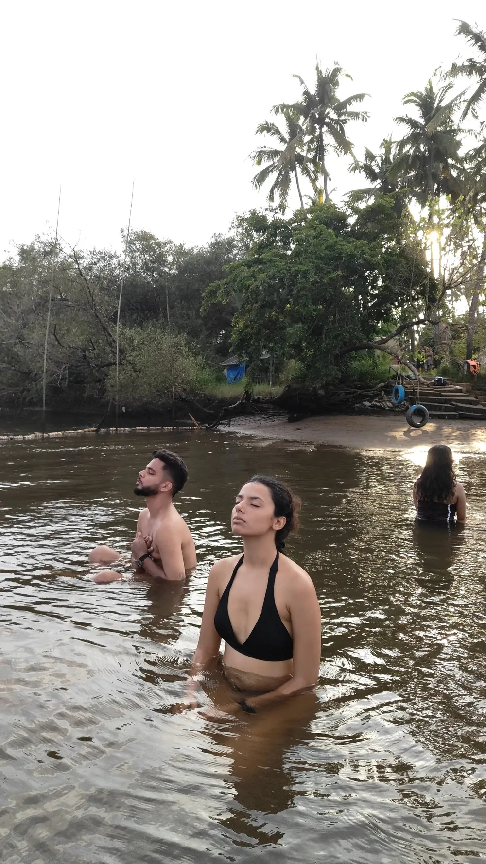 Two guests with eyes closed breathing slowly, waist-deep in the river at golden hour